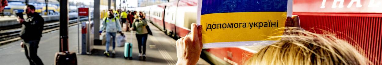 Een vrouw houdt een papier met de Oekraïense vlag vast om vluchtelingen op het treinstation te verwelkomen