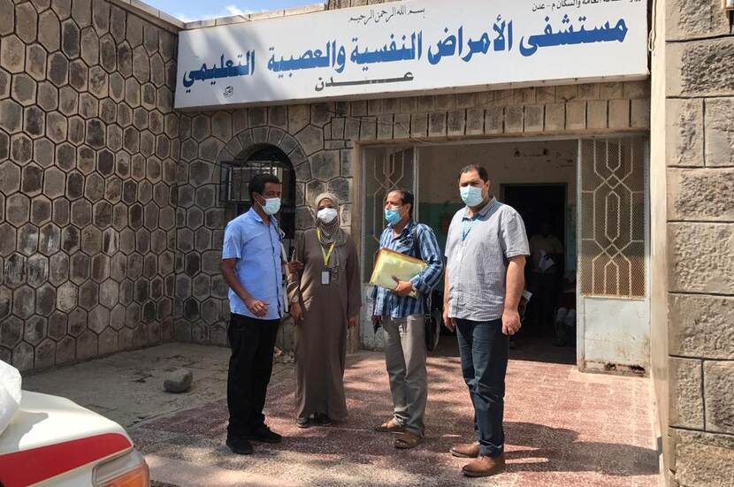 Drie mannen en vrouw met mondkapje voor gebouw met arabisch schrift