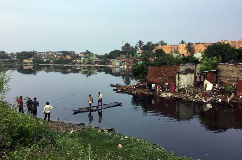 Mensen aan de waterkant en op een boot op de rivier die langs een sloppenwijk voert
