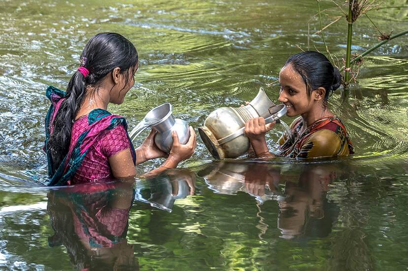 Twee meisjes in Bangladesh spelen in het water met hun waterkannen